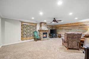 Carpeted living room with crown molding, recessed lighting, ceiling fan, and a stone fireplace