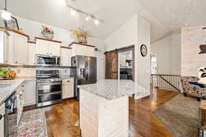 Kitchen featuring stainless steel appliances, a barn door, light stone counters, a center island, and dark wood-style floors