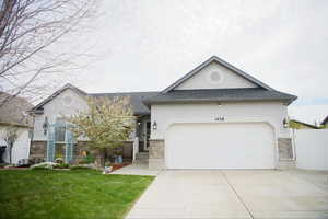 View of front facade featuring stone siding, roof with shingles, concrete driveway, and stucco siding