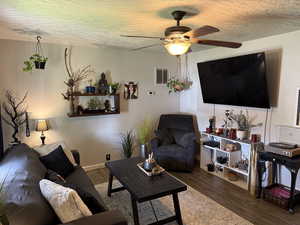 Living room with dark wood-style flooring, a textured ceiling, and ceiling fan