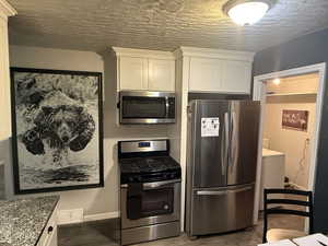 Kitchen featuring stainless steel appliances, dark wood-style flooring, light stone countertops, washer / dryer, and a textured ceiling