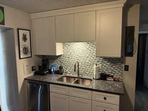 Kitchen with stainless steel dishwasher, white cabinetry, dark stone counters, and tasteful backsplash