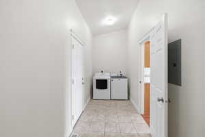 Laundry room with electric panel, independent washer and dryer, light tile patterned floors, and lofted ceiling
