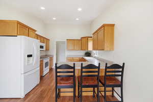 Kitchen with a peninsula, white appliances, a breakfast bar, light countertops, and light wood finished floors