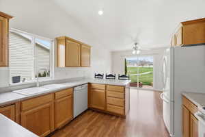 Kitchen with light countertops, light wood finished floors, white appliances, vaulted ceiling, and a peninsula