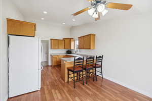 Kitchen with a peninsula, freestanding refrigerator, wood finish cabinets, a kitchen breakfast bar, and lofted ceiling