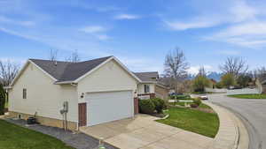View of side of property with a lawn, an attached garage, driveway, brick siding, and roof with shingles