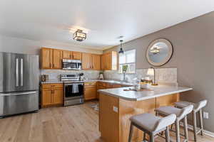 Kitchen featuring stainless steel appliances, a breakfast bar area, a peninsula, light countertops, and light wood-style floors