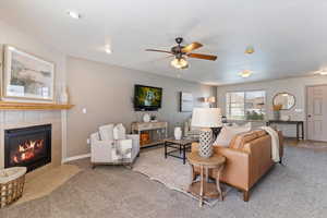 Carpeted living room featuring ceiling fan and a tiled fireplace