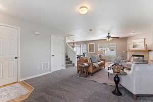 Carpeted living room featuring a tile fireplace and a ceiling fan
