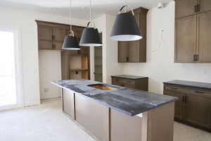 Kitchen featuring an island with sink, wood finish cabinetry, and decorative light fixtures
