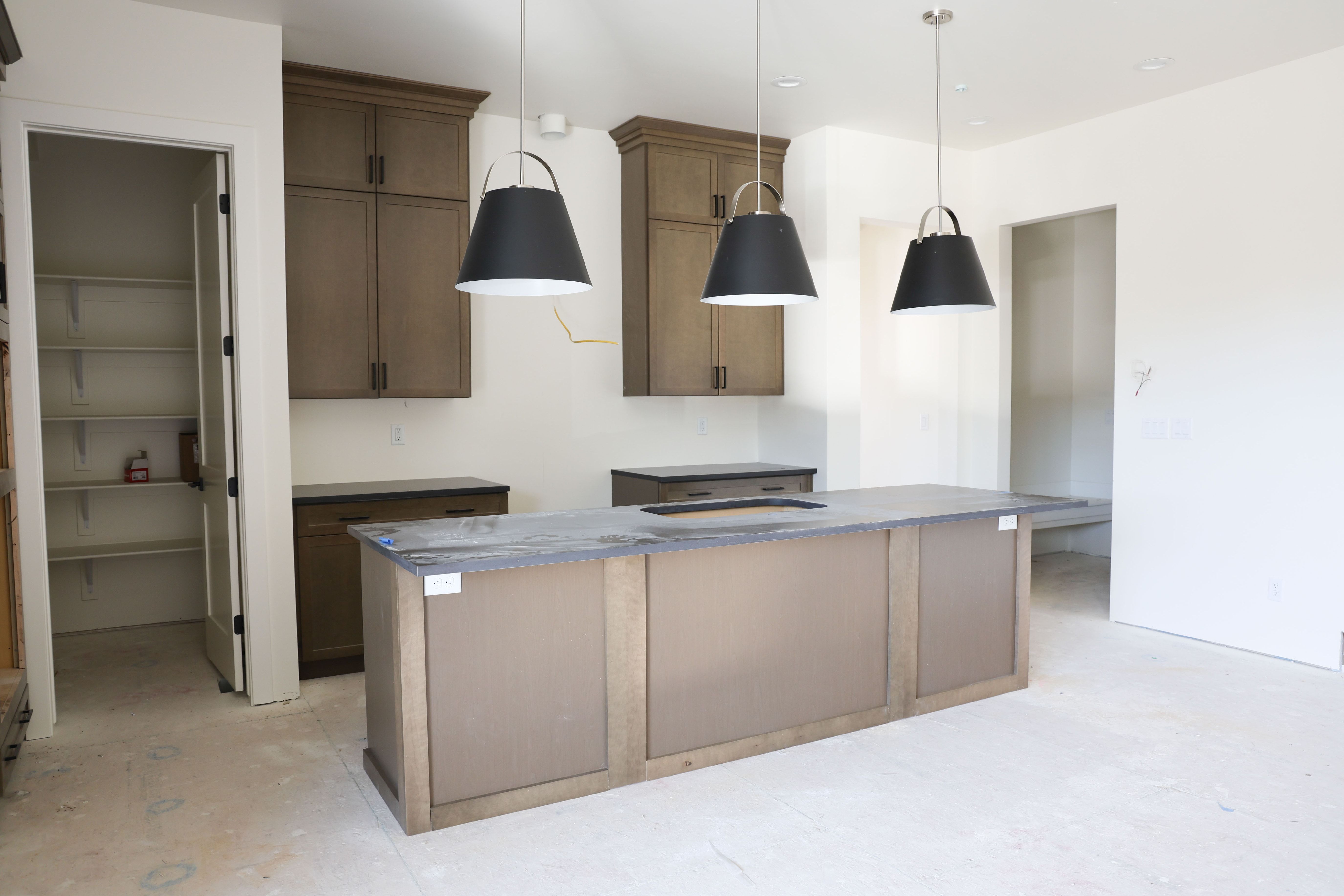 Kitchen featuring a kitchen island with sink, decorative light fixtures, wood finish cabinets, and concrete floors