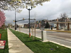 View of asphalt road featuring a residential view, sidewalks, curbs, traffic lights, and street lighting