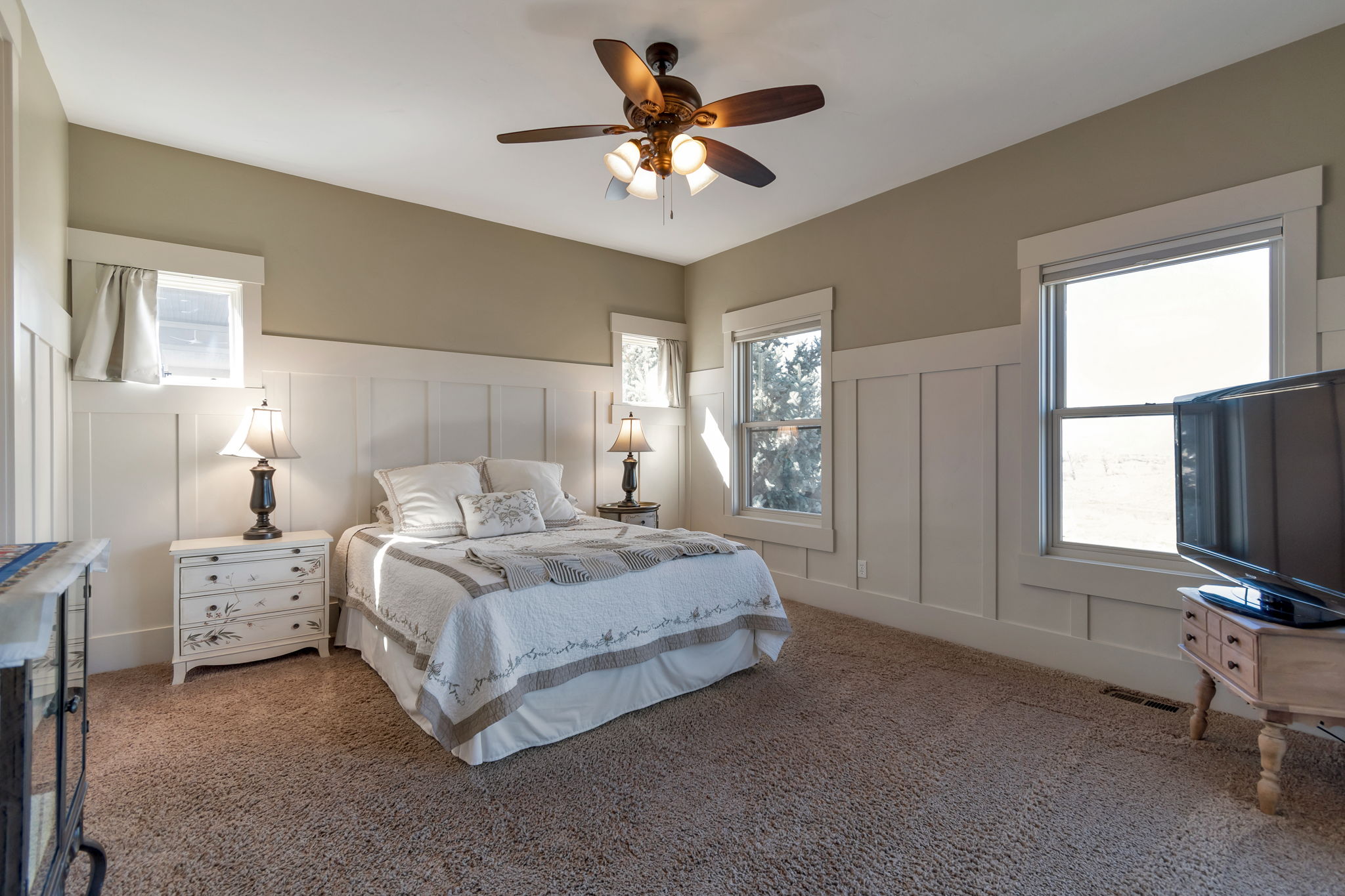 Carpeted bedroom featuring a decorative wall, ceiling fan, and wainscoting
