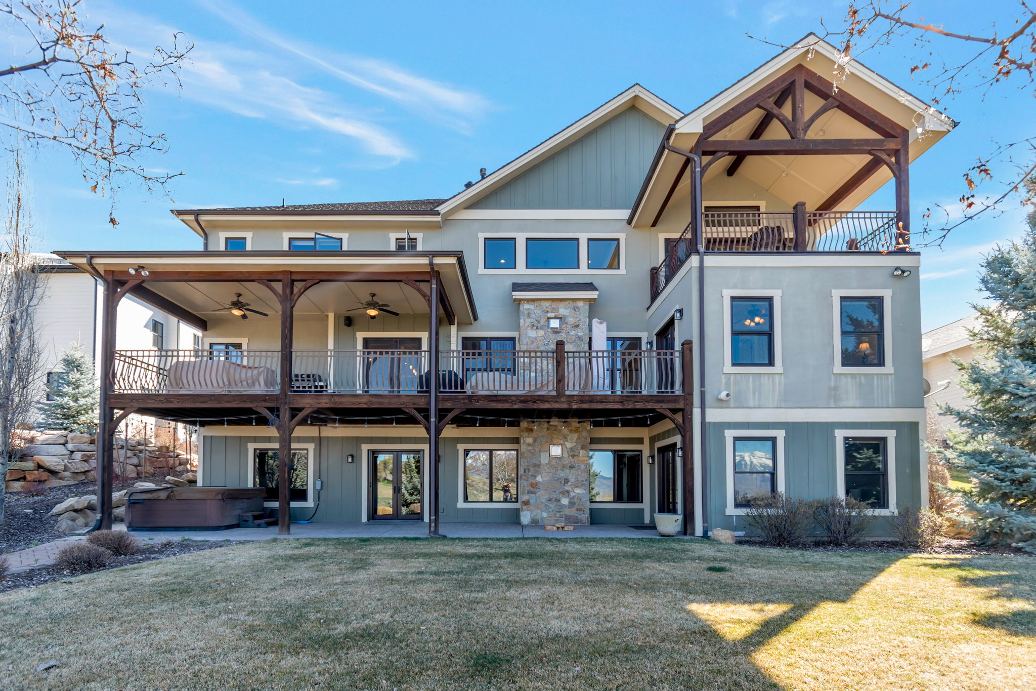 Rear view of house featuring a patio, a hot tub, a ceiling fan, a yard, and stone siding