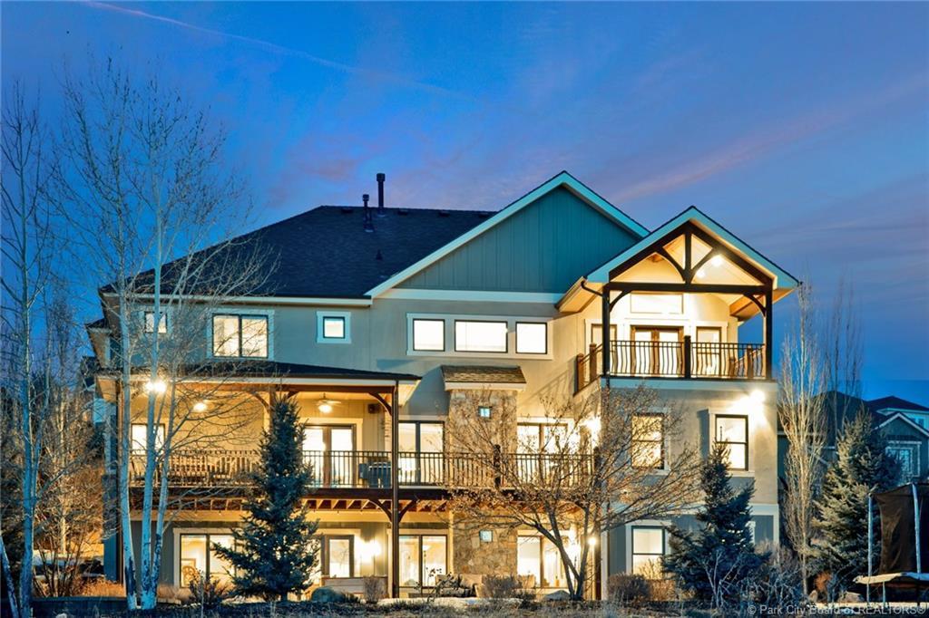 Back of property at dusk featuring a balcony, a trampoline, stone siding, stucco siding, and a patio area