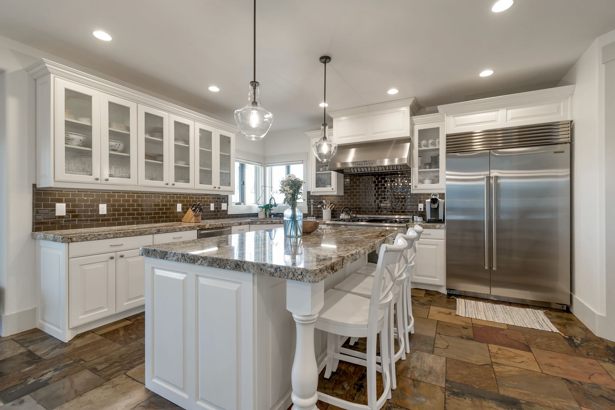 Kitchen with glass fronted cabinets, stainless steel built in refrigerator, white cabinets, a breakfast bar, and pendant lighting