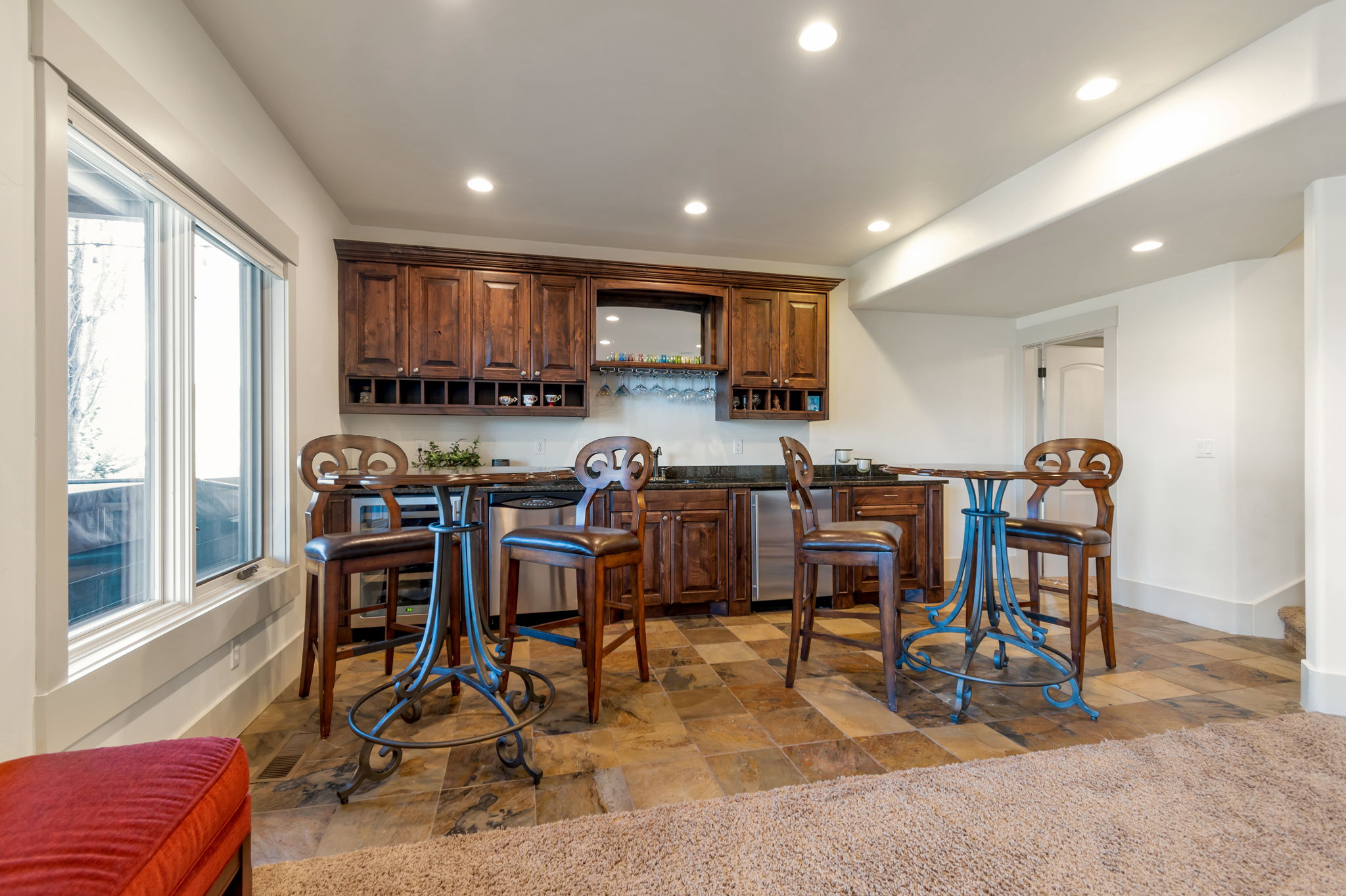 Indoor wet bar with light stone finish flooring, recessed lighting, stainless steel dishwasher, dark stone countertops, and dark wood finish cabinets