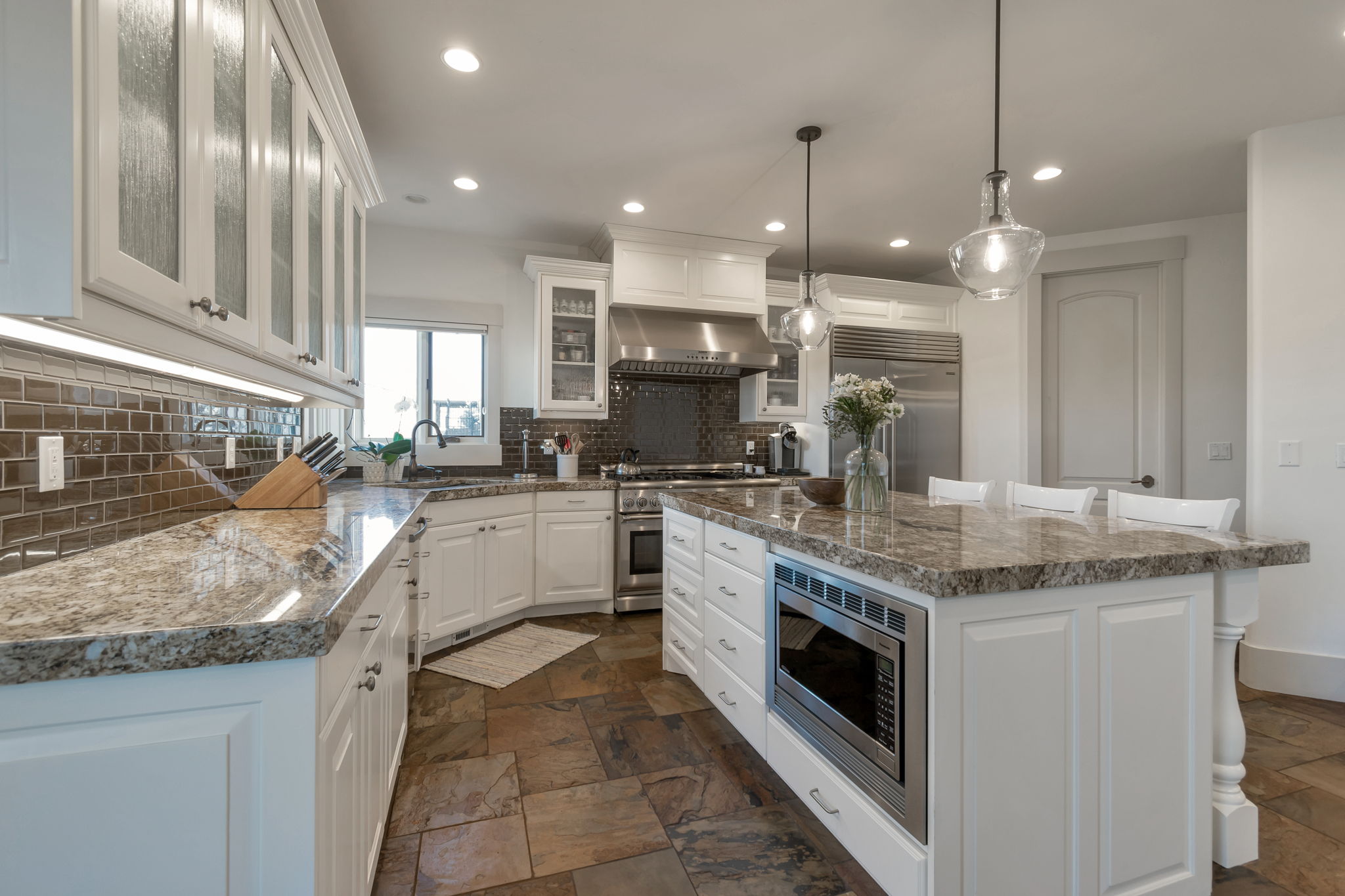 Kitchen featuring white cabinets, glass insert cabinets, built in appliances, and stone tile flooring