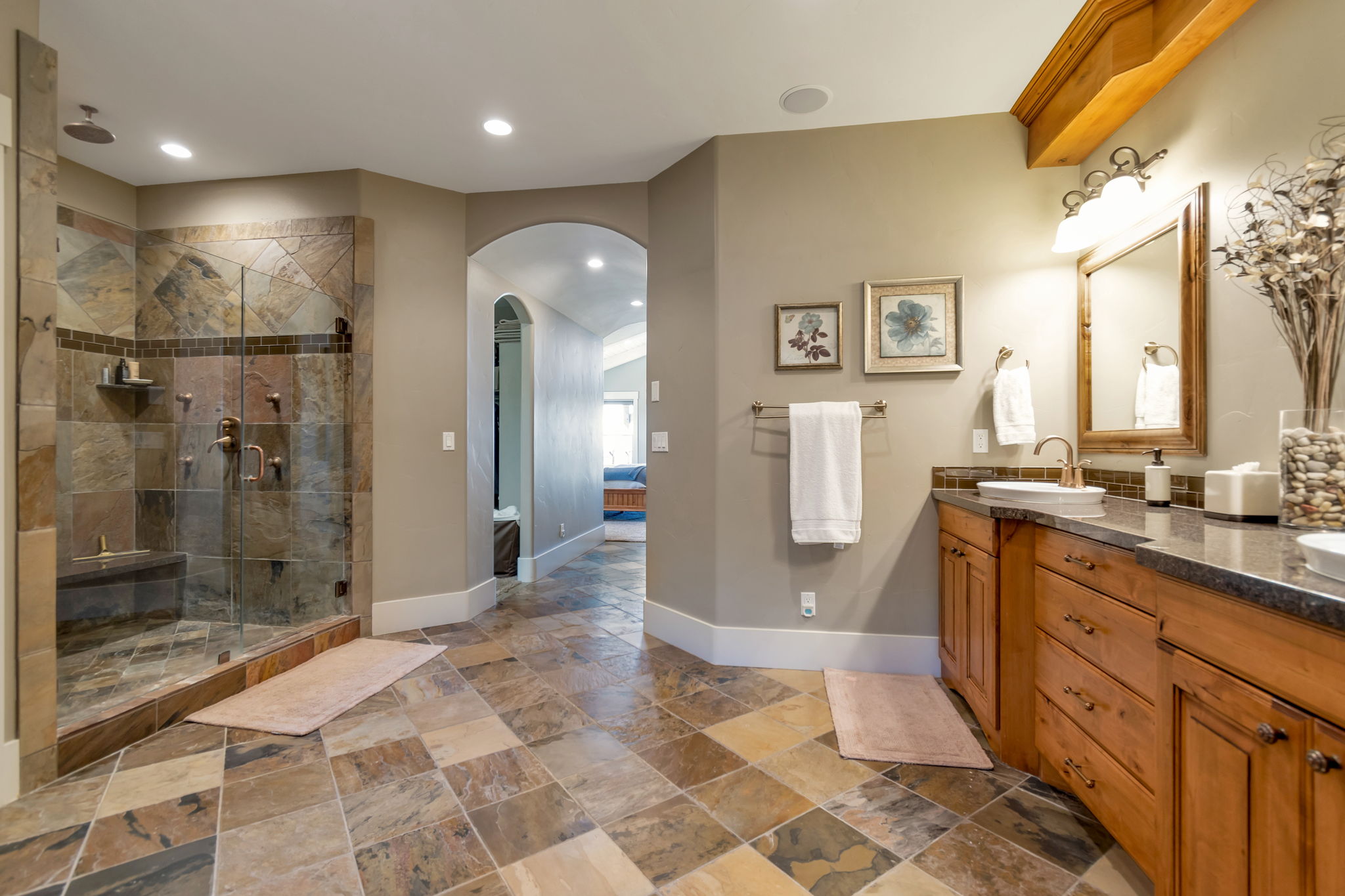 Ensuite bathroom with double vanity, a shower stall, stone tile flooring, and recessed lighting