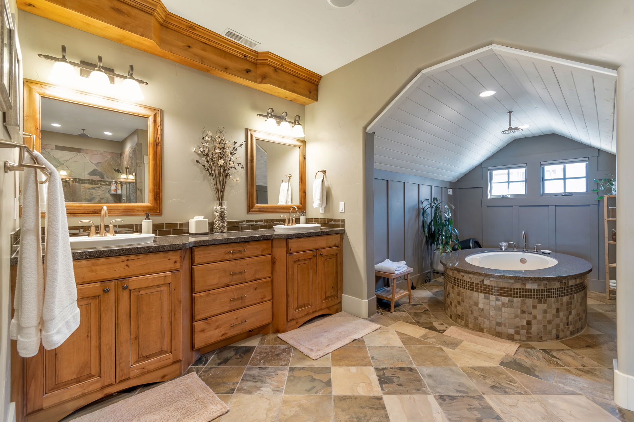 Bathroom with double vanity, lofted ceiling, stone tile floors, a walk in shower, and a bath