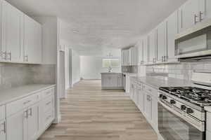 Kitchen featuring stainless steel appliances, decorative backsplash, light wood-type flooring, a peninsula, and white cabinetry