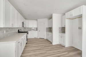 Kitchen featuring gas range, white cabinetry, light wood-type flooring, decorative backsplash, and a textured ceiling