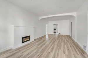 Unfurnished living room featuring arched walkways, a glass covered fireplace, and light wood-type flooring