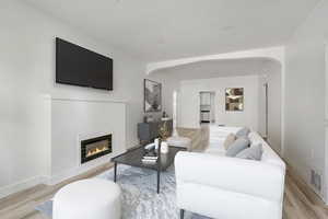Living area featuring arched walkways, a glass covered fireplace, and light wood-style floors