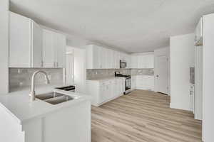 Kitchen featuring stainless steel appliances, a peninsula, white cabinetry, light wood-style flooring, and tasteful backsplash