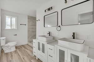 Bathroom with double vanity, light wood-style floors, and tiled shower