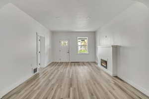 Unfurnished living room featuring a glass covered fireplace and light wood-style flooring