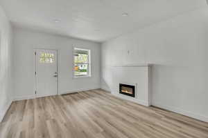 Unfurnished living room featuring light wood-style floors, a glass covered fireplace, and recessed lighting