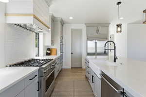 Kitchen pantry with gray cabinetry, stainless steel appliances, decorative light fixtures, light stone counters, and light wood finished floors