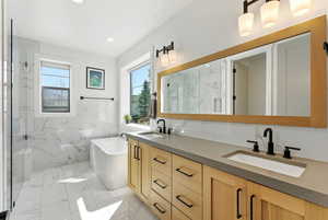 Primary Bathroom with double vanity, a freestanding bath, a marble finish shower, light marble finish flooring, and recessed lighting