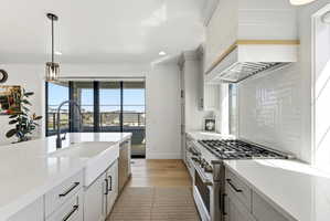Kitchen & front balcony featuring stainless steel range, decorative light fixtures, light stone countertops, light wood finished floors, and tasteful backsplash