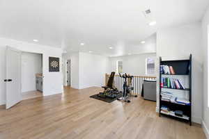 Exercise room with light wood-style floors and recessed lighting