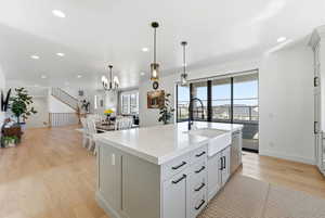 Kitchen featuring light wood finished floors, light stone countertops, a center island with sink, white cabinetry, and open floor plan