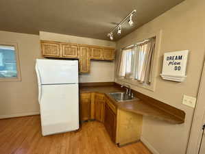 Kitchen featuring freestanding refrigerator, dark countertops, rail lighting, light wood-style floors, and wood finish cabinetry