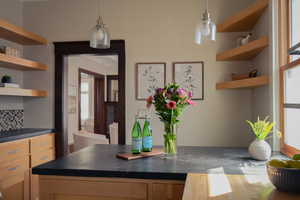Kitchen with open shelves, dark countertops, light wood finish cabinetry, and decorative backsplash
