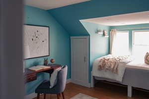 Bedroom featuring wood finished floors, lofted ceiling, and an office area