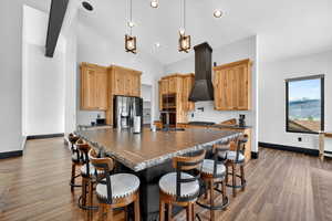 Kitchen with an island with sink, a breakfast bar, hanging light fixtures, dark wood-style flooring, and stainless steel appliances