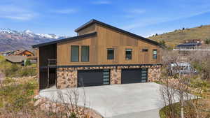 Contemporary home with an attached garage, a mountain view, stone siding, and concrete driveway