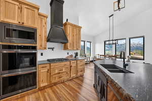 Dual tone kitchen with stainless steel appliances, lofted ceiling, dark stone counters, a chandelier, and light wood-type flooring