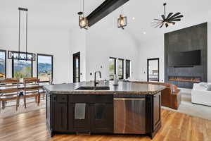 Kitchen featuring stainless steel dishwasher, a fireplace, a kitchen island with sink, open floor plan, and dark countertops