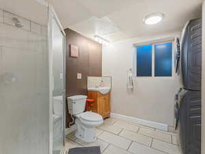 Full bathroom with vanity, a stall shower, stacked washer / drying machine, and light tile patterned floors