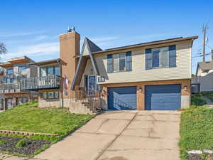 View of front of property featuring an attached garage, driveway, brick siding, a front yard, and a chimney