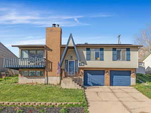 View of front facade featuring brick siding, a front yard, concrete driveway, a chimney, and a garage