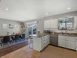 Kitchen with white cabinets, a peninsula, stainless steel appliances, light tile patterned flooring, and a kitchen bar