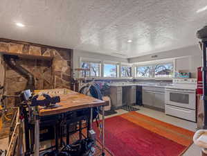 Kitchen featuring a textured ceiling, white electric stove, gray cabinets, light countertops, and a wood stove
